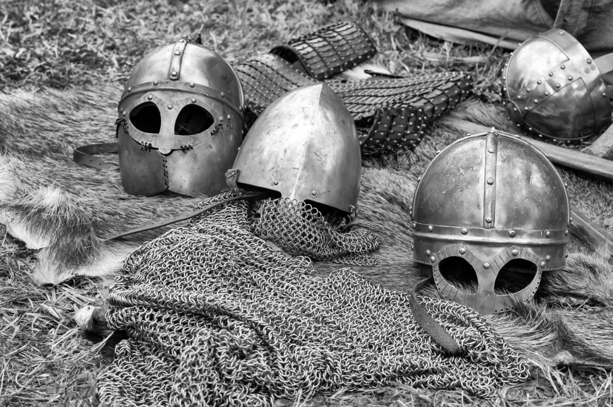 Image of three medieval helmets resting on a swathe of chainmail,